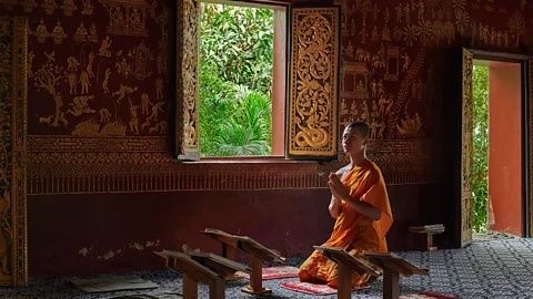 Buddhistisk munk sidder i meditation i et rigt dekoreret rum