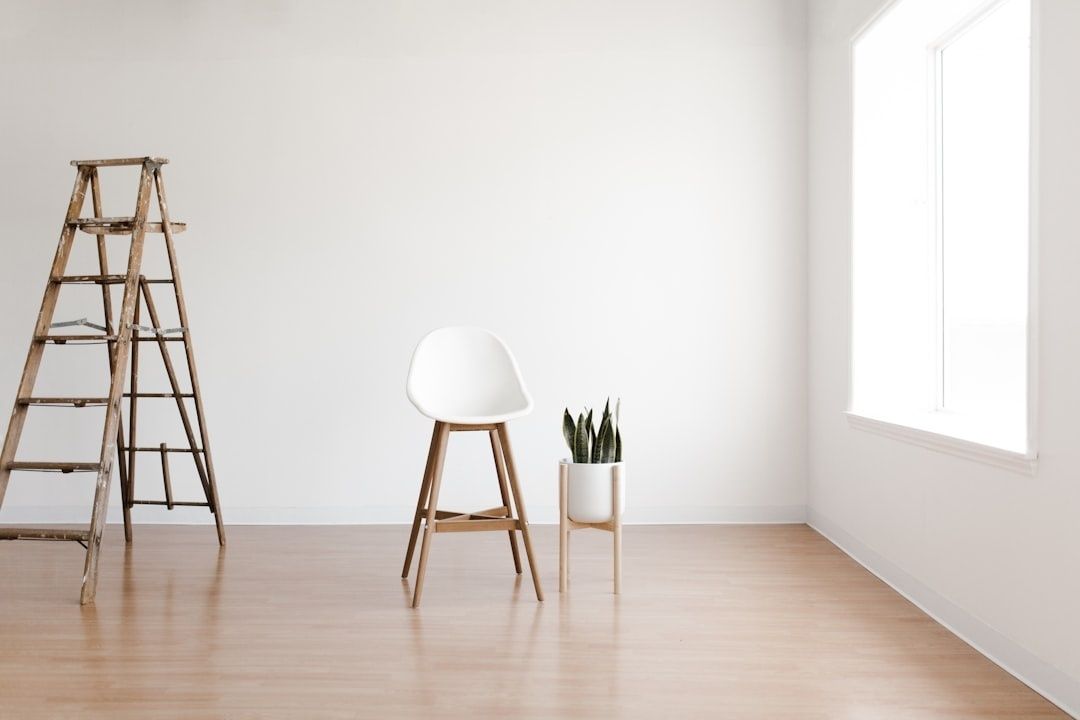Lyst, minimalistisk rum med stige, stol og plante i stilhed